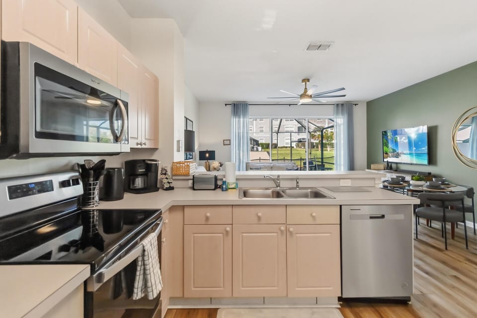 Stainless steel appliances and light wood cabinets frame the kitchen with a double sink overlooking the living area.