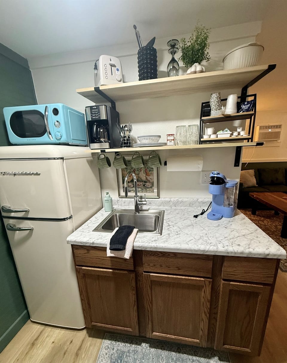Kitchenette with a coffee maker, coffee supplies, toaster, microwave, fridge with a freezer, and a few dishes and utensils. 