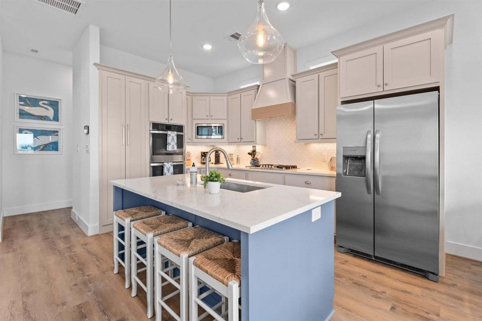 Spacious kitchen with oversized island, bar stools, stainless steel refrigerator and custom cabinetry.