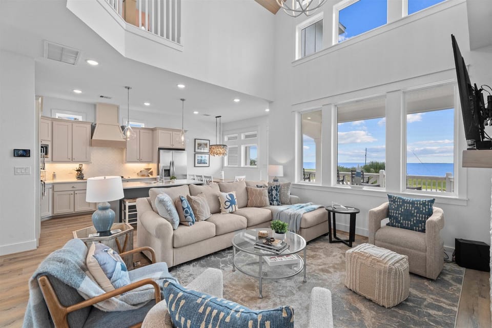Open living and kitchen area with luxury furnishings, coastal decor and expansive natural lighting.
