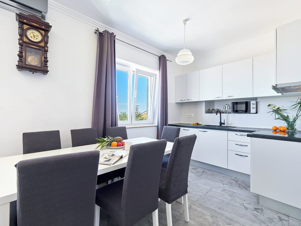 This bright, modern kitchen boasts sleek white cabinetry. Gather at the elegant dining table beneath a unique vintage wall clock.
