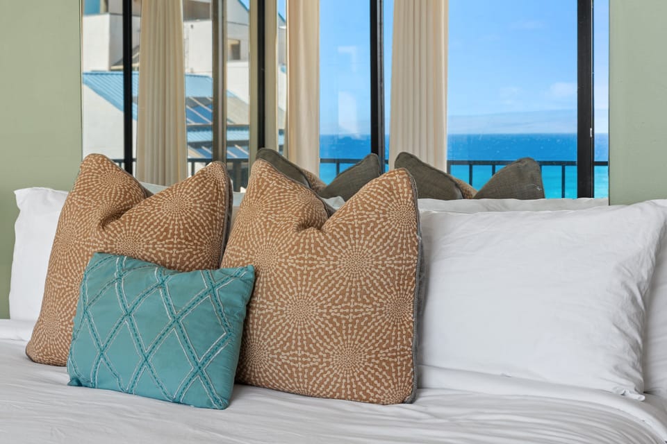 Plush bedding with decorative pillows in a bright ocean-view bedroom.