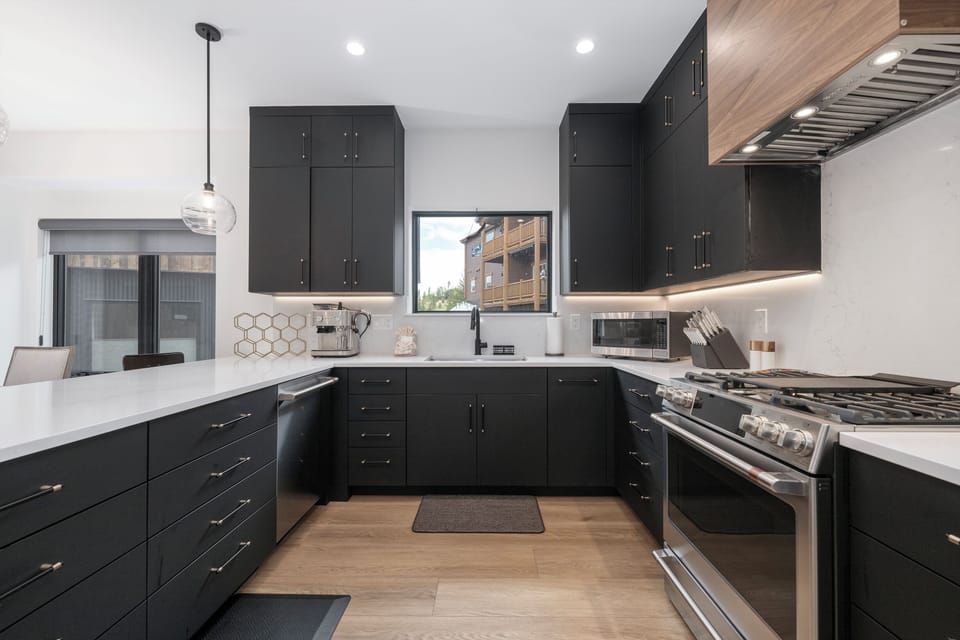 Step into your modern chef's kitchen with sleek charcoal cabinetry, crisp white countertops, and high-end appliances. Ample prep space and warm wood-tone flooring invite you to cook and create in style.