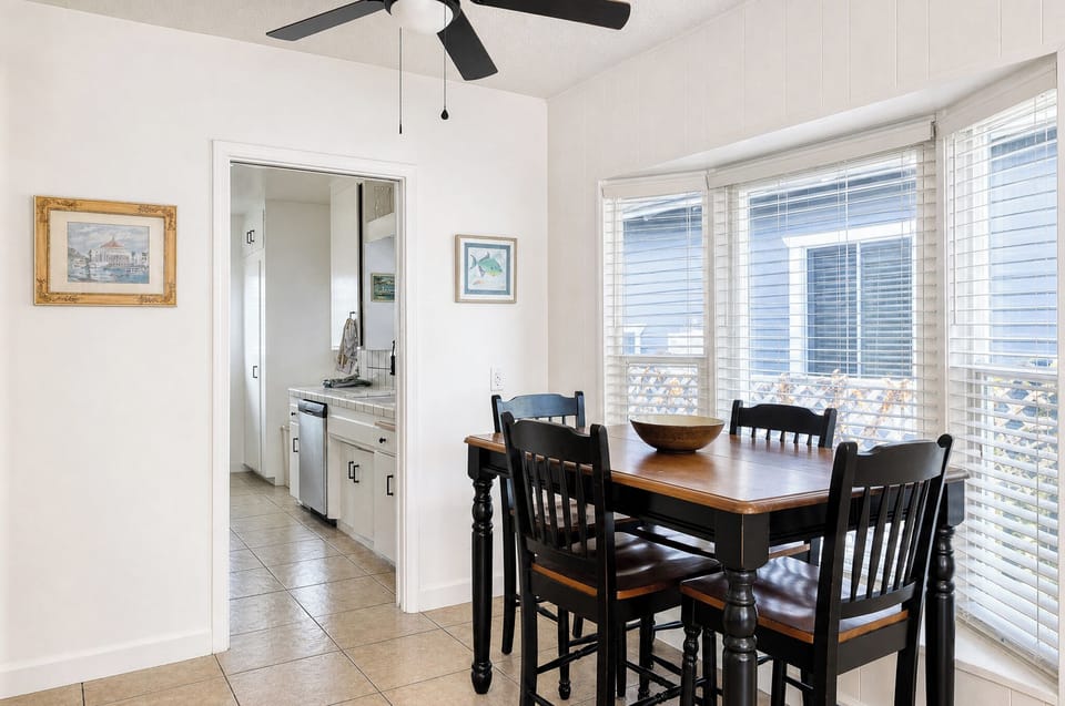 Gather around this inviting dining table where you can share meals and stories while natural light streams through large windows, keeping your space bright and airy with ceiling fan comfort.