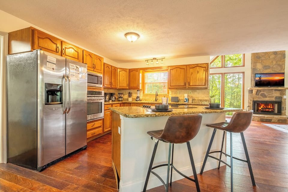Your fully-equipped kitchen features a welcoming breakfast bar for casual meals, with forest views and a cozy fireplace creating a warm mountain retreat atmosphere.