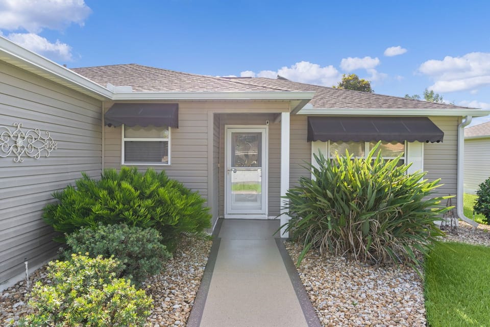 The property features a welcoming single-story structure with neutral siding, decorative awnings, and mature landscaping, set in a peaceful residential neighborhood.