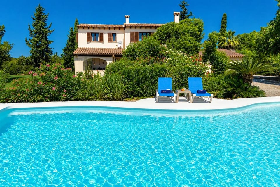 A stunning villa pool surrounded by lush gardens, blue loungers, and Mediterranean charm.