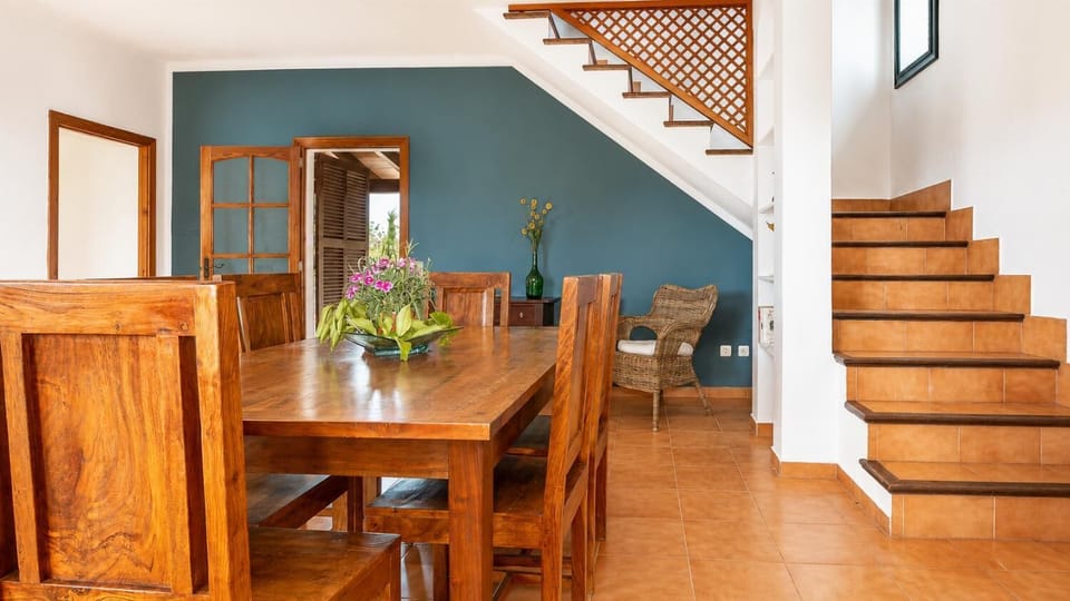 A rustic dining area with wooden furniture, warm tiled floors, and a charming staircase.