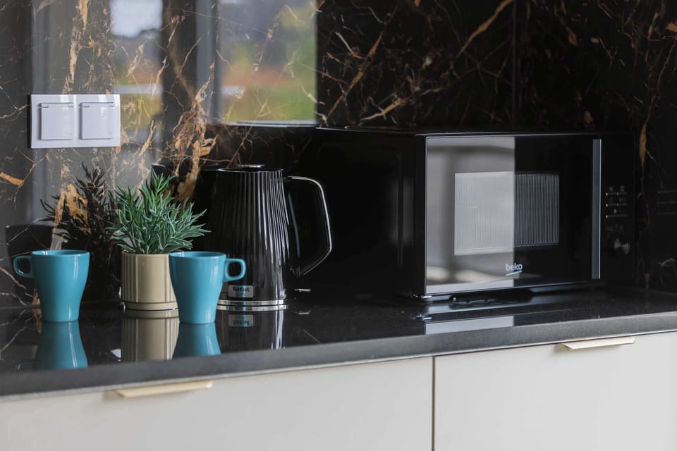 A kitchen countertop with small appliances and decorative plants. Dark finishes add a contemporary touch.