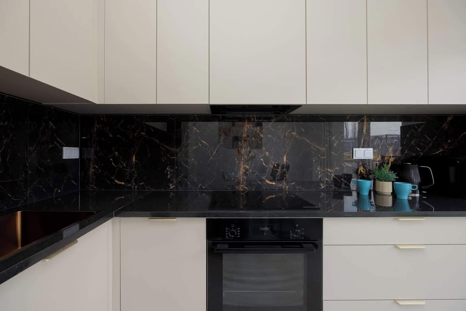 A modern kitchen with white cabinets and a black backsplash. Built-in appliances give the space a sleek look.