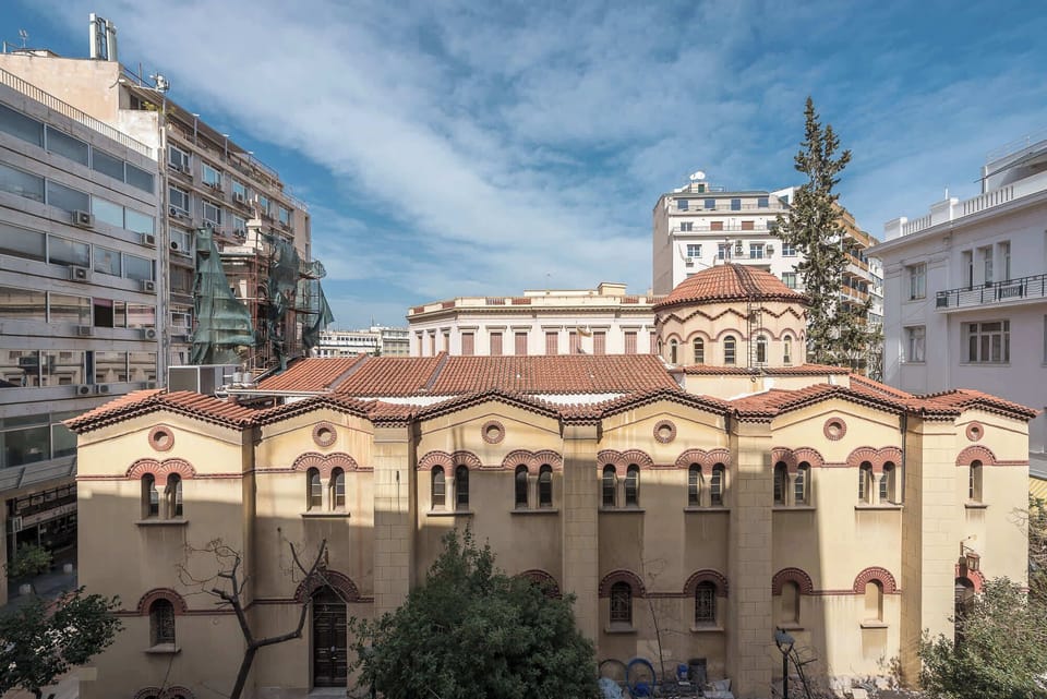 Elevated city outlook showcasing historic church architecture, central Athens rooftops, and open skies beyond window.