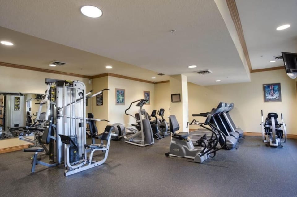 Exercise machines, including treadmills and a multi-station weight machine, fill a carpeted fitness room.