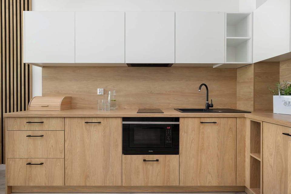 A functional kitchenette with wood-grain base cabinets and white upper cabinets. The countertop features a sink, a stovetop, and small kitchen accessories.