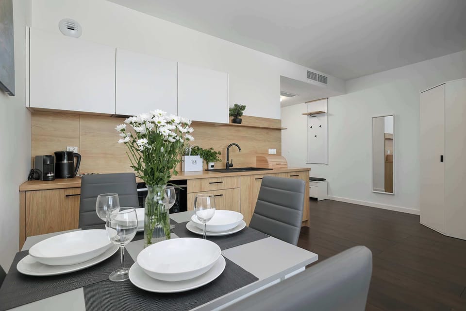 An elegant kitchenette with a white dining table and chairs in the foreground. A complete dinner set for guests has been laid out on the table.