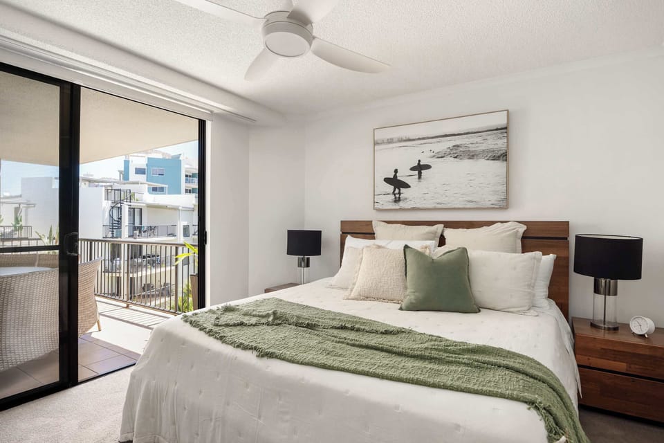 Relax in the master bedroom featuring a king bed, ceiling fan and direct access to the balcony — a calm, light-filled retreat.