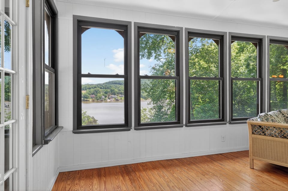 Bright sunroom-style space with large windows showcasing peaceful lake and tree-lined views.