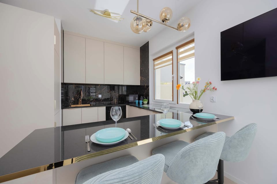 A modern dining bar features a glossy black countertop paired with stylish light blue velvet chairs. A sophisticated multi-bulb golden light fixture hangs from the ceiling above the dining area.