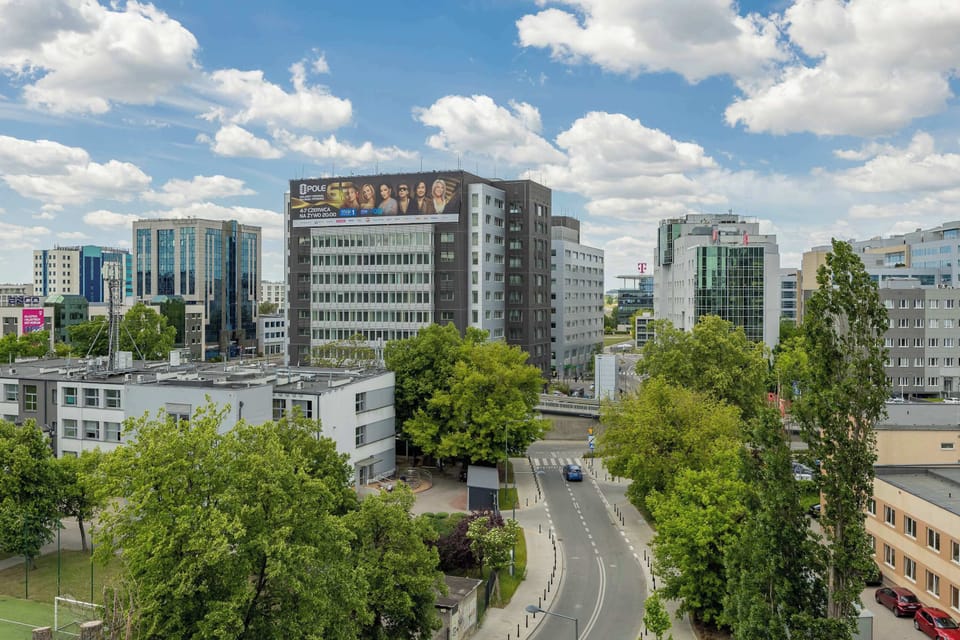 An elevated perspective showcases a winding city street lined with lush green trees and modern office buildings. The vibrant neighborhood looks clean, well-maintained, and accessible.