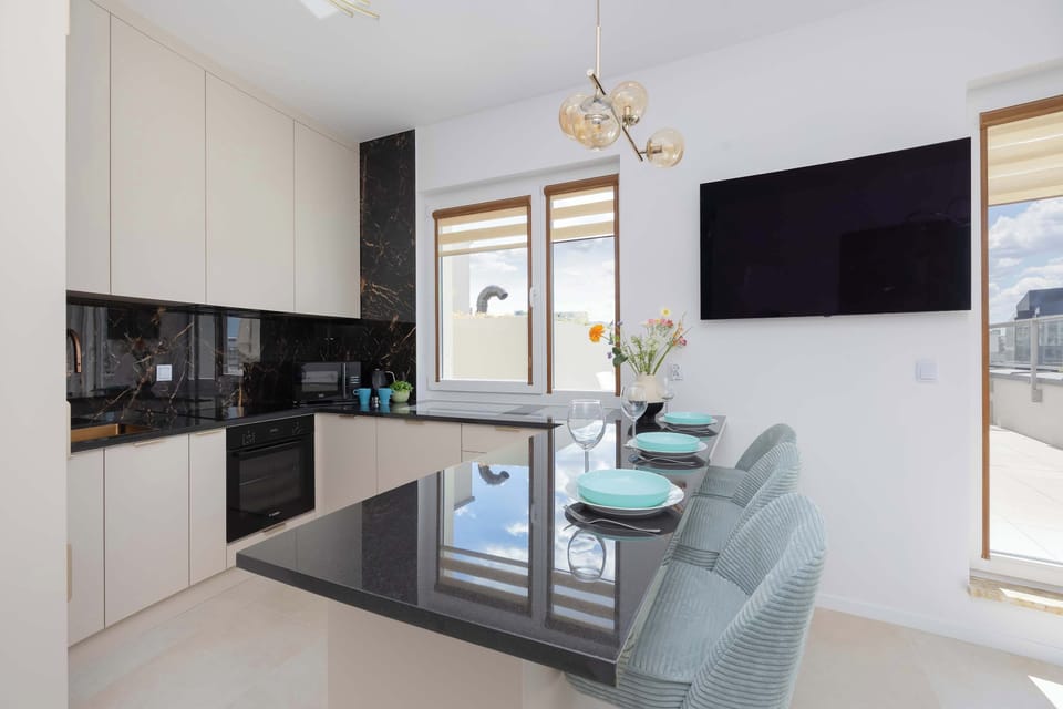 The kitchenette area is presented with its sleek dark countertops and modern appliances. A large flat-screen TV is perfectly positioned on the adjacent wall for entertainment while cooking or dining.