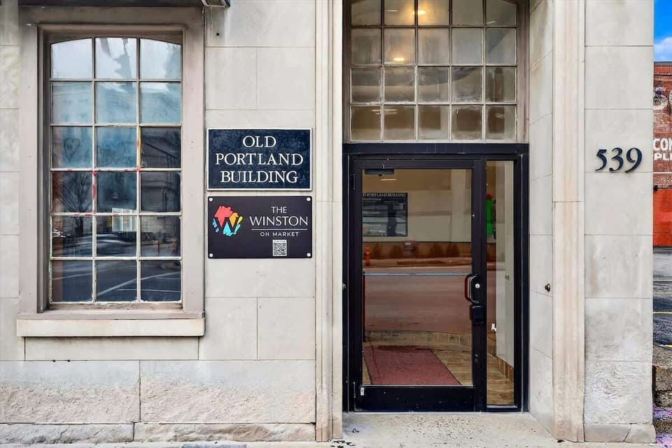 Enter through the vestibule featuring the original stone facade and modern glass doors. The signage clearly marks your arrival at the building.