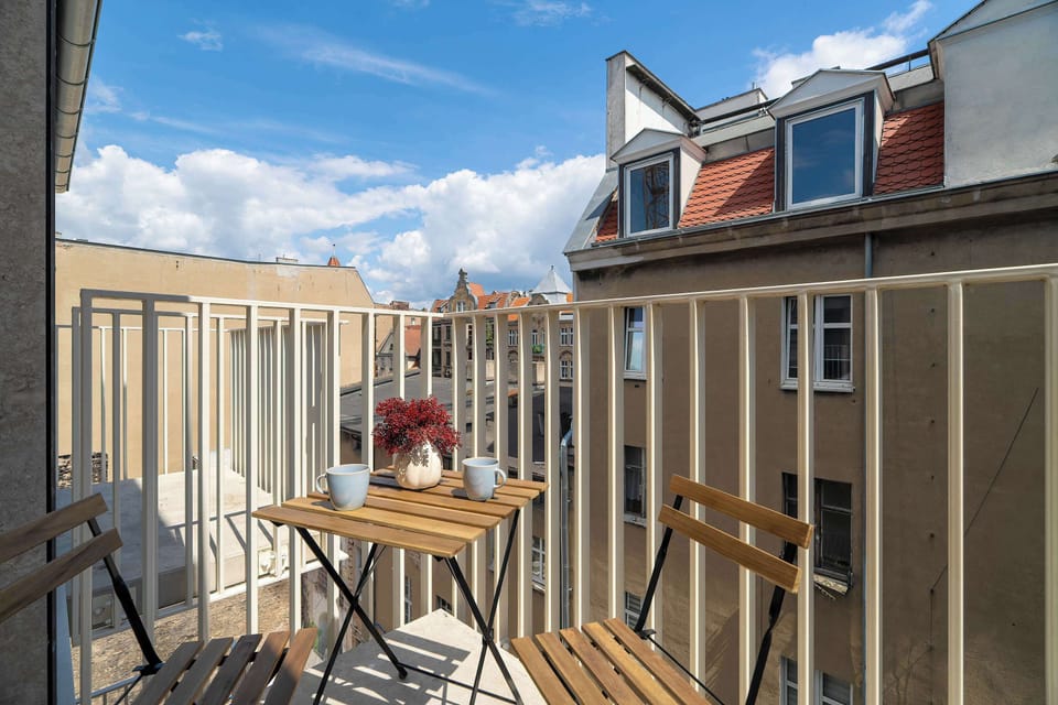 A small private balcony with outdoor seating and a view of surrounding buildings. It offers a pleasant spot to enjoy fresh air in an urban setting.