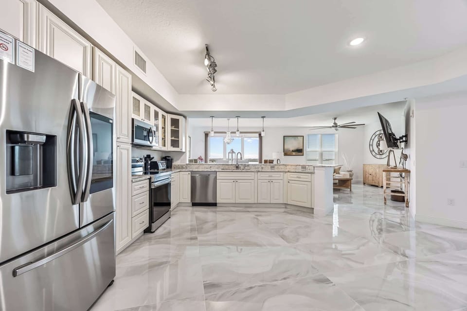 Modern kitchen with stainless steel appliances and marble flooring overlooking the living area.
