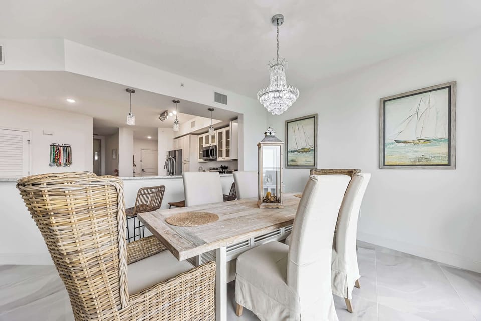 Dining area with a rustic wooden table, wicker and upholstered chairs, and a crystal chandelier.