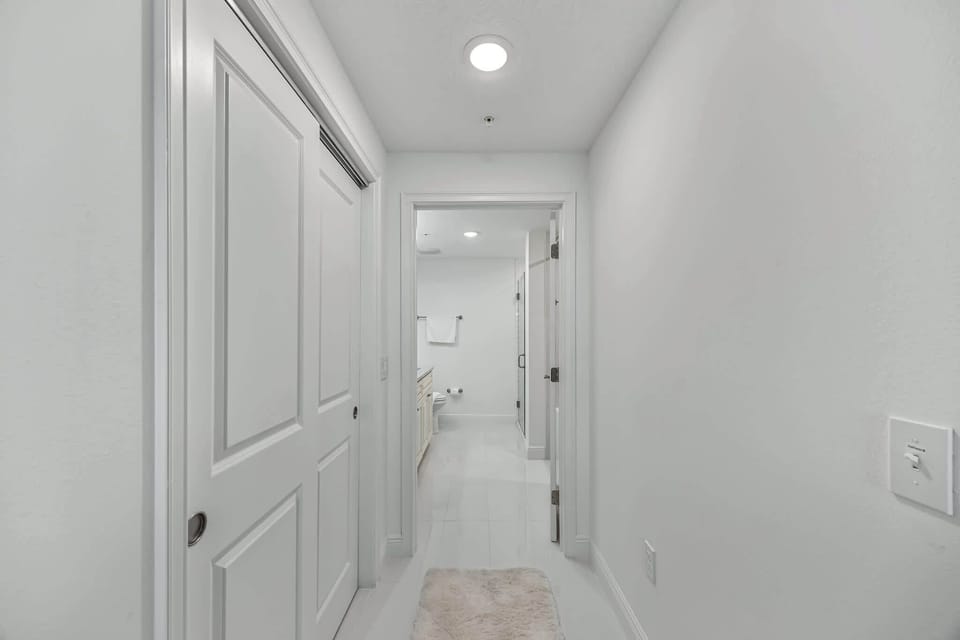 hallway leading to a modern bathroom with white walls and tile flooring