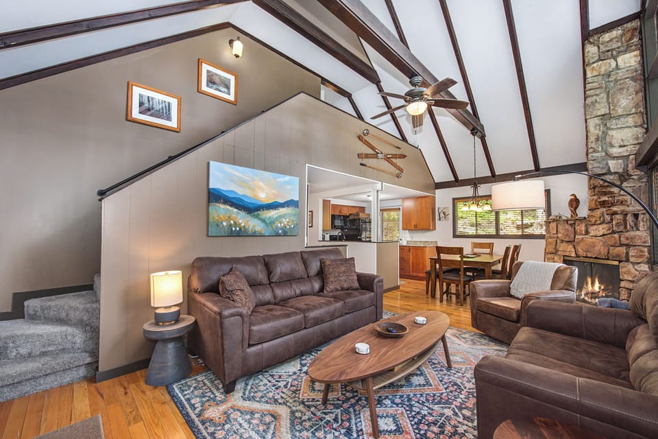Settle into this welcoming living space with soaring vaulted ceilings, leather seating around the fireplace, and an open layout that flows naturally into the dining and kitchen areas.