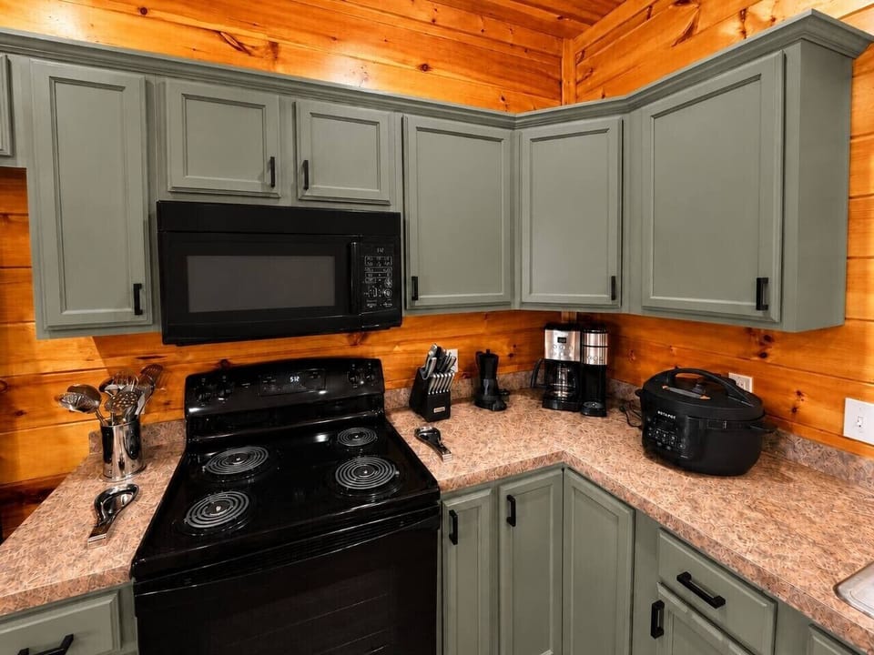 Fully equipped Gatlinburg cabin kitchen with stove, microwave, coffee makers, cookware, and modern sage green cabinets.