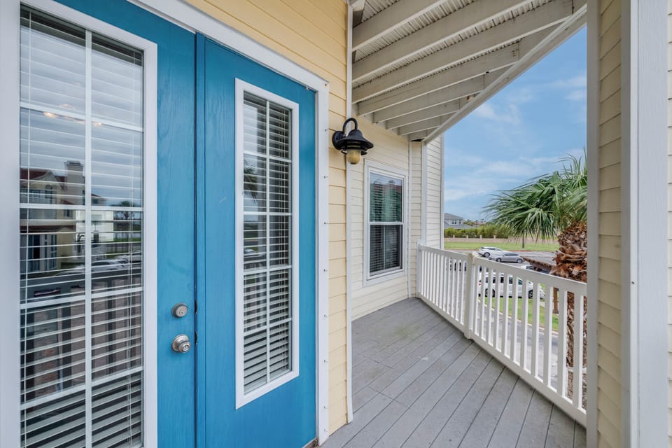 The property welcomes you with coastal charm—this inviting front porch features a charming blue door, nautical-style lighting, and views of palm-dotted surroundings. A perfect start to your beachside escape.
