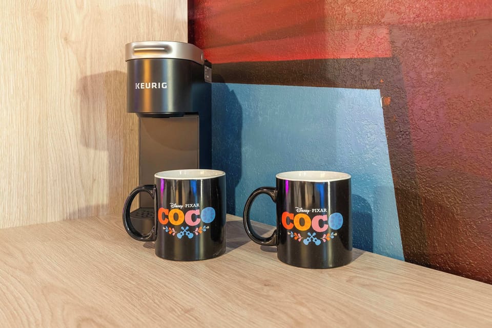 Compact keurig coffee maker with two disney pixar coco mugs on a wooden countertop