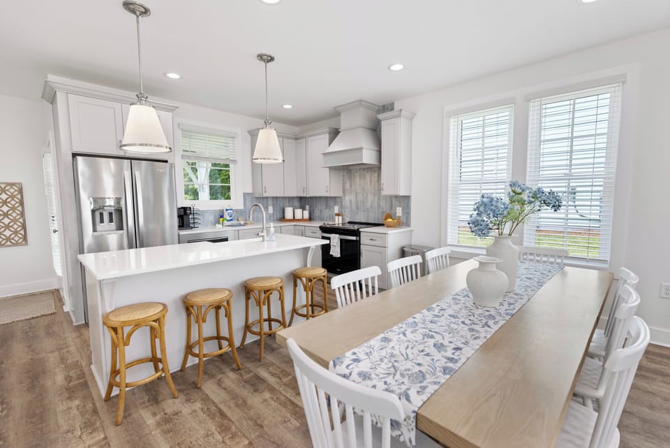 Gather around the bright kitchen island for morning coffee or host dinners at the elegant table—white cabinetry, modern appliances, and cheerful natural light make meal prep feel effortless and inviting.