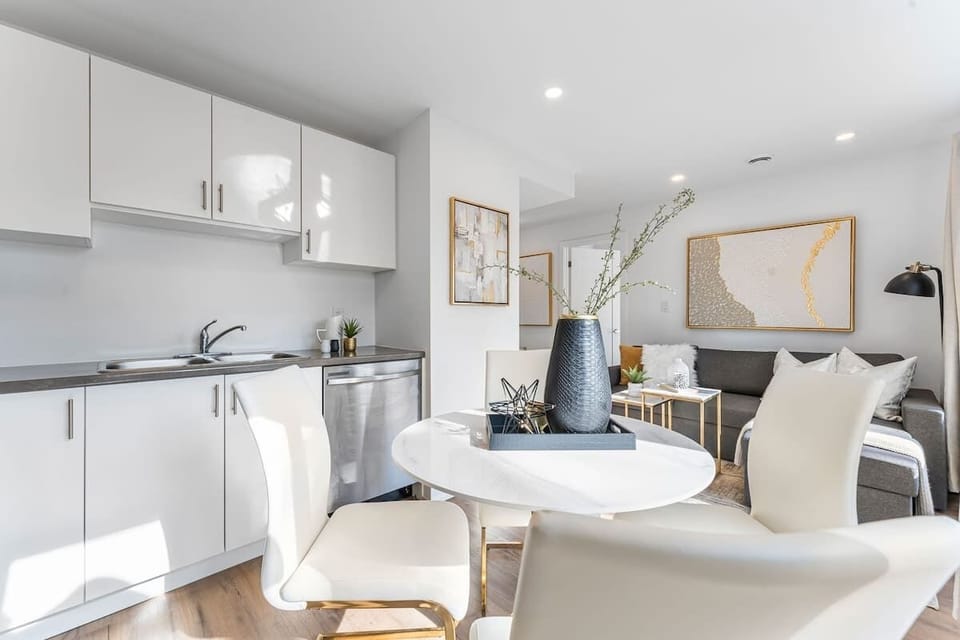 Bright open living area with modern kitchen, cozy sectional, dining table, and large windows.