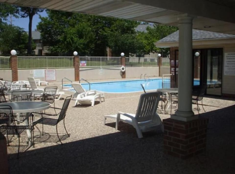 Outdoor pool area features white plastic loungers and black metal tables with chairs on textured concrete.
