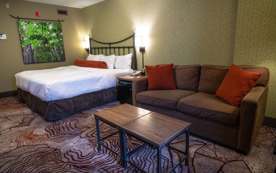 Upper-floor king room with warm wood tones and earthy décor — private balcony just through the door