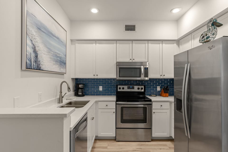 Step into your fully equipped kitchen featuring sleek stainless steel appliances, modern white cabinetry, and stylish blue subway tile backsplash—perfect for preparing your favorite meals during your stay.