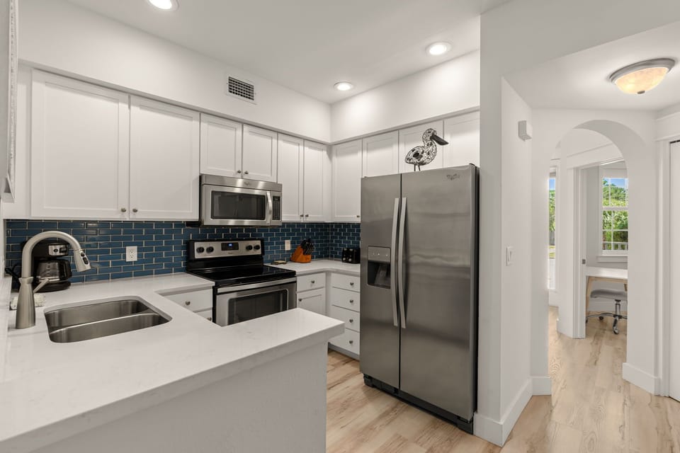 Your fully equipped kitchen awaits with sleek white cabinetry, stainless steel appliances, and a chic blue backsplash. Meal prep is effortless on spacious quartz counters.