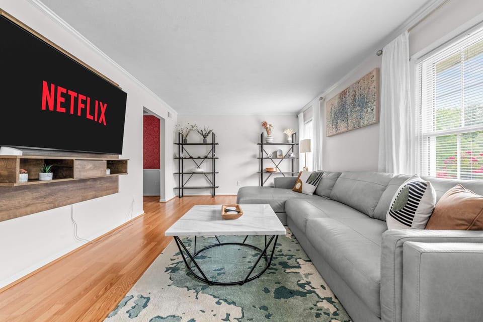 The massive wall-mounted smart TV is ready for your favorite Netflix series, complete with a custom floating wooden media console and minimalist decor accents.