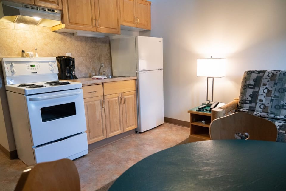 Close-up of the kitchen counter: black-top stove, coffee maker, and sink with log-style seating nearby