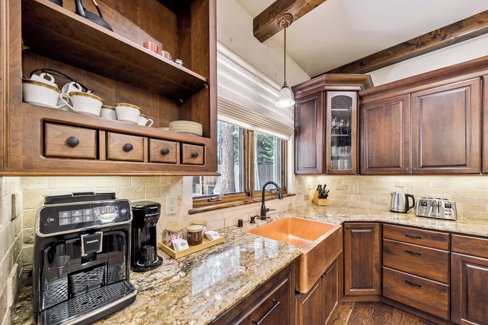 Your fully equipped kitchen blends rustic charm with modern convenience, featuring rich wood cabinetry, exposed beams, granite counters, and a copper farmhouse sink for memorable meal prep.