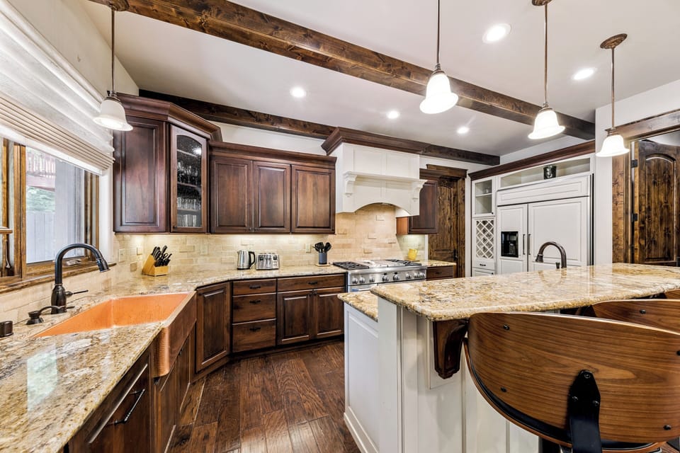 Gather around this stunning kitchen where rustic wood beams meet modern convenience. Gleaming granite countertops and chef-grade appliances make meal prep a joy, while the spacious island invites you to linger over morning coffee.