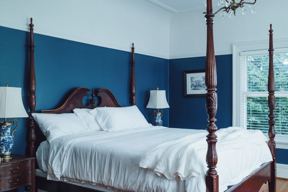Elegant four-poster bedroom with bold blue walls and natural light