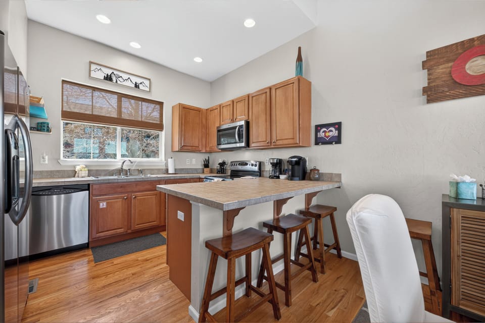 Cook your favorite meals in this fully equipped kitchen featuring modern appliances, breakfast bar seating, and charming mountain views through the window.