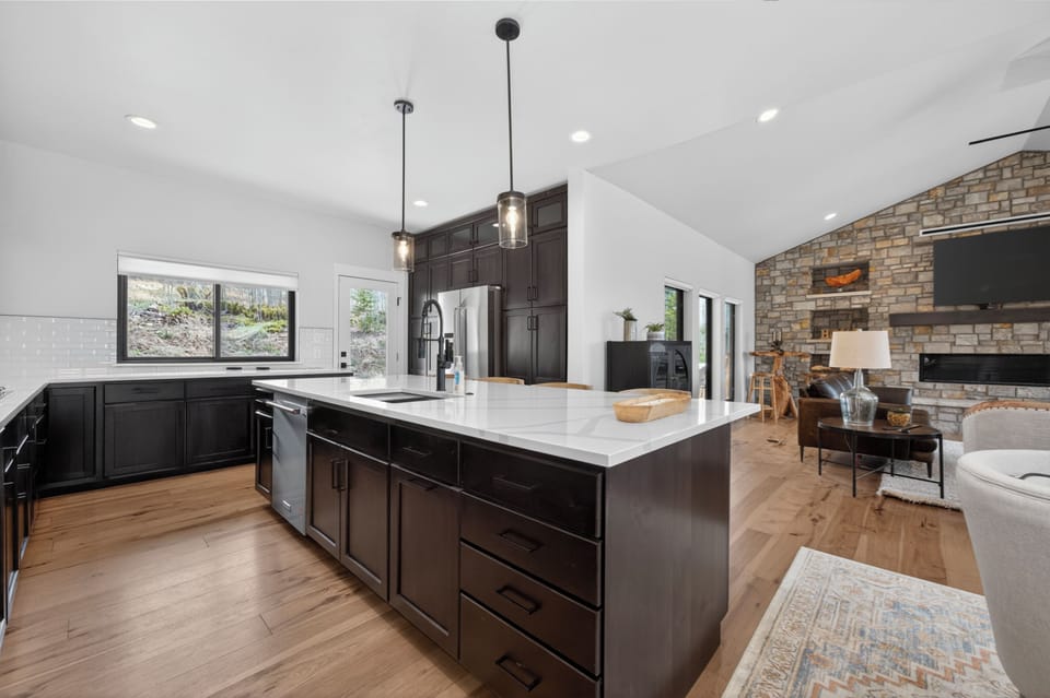 Sleek kitchen with pristine countertops flows into a warm living area with stone fireplace—your perfect space for gathering and entertaining in mountain-modern style.