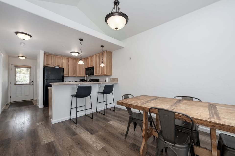 Your open-concept kitchen and dining space welcomes you with warm wood finishes, modern black appliances, and a rustic farmhouse table perfect for shared meals and morning coffee.