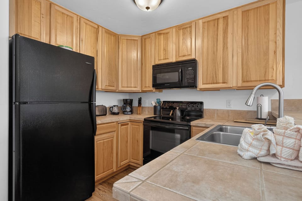 Your fully equipped kitchen features warm wood cabinetry, modern black appliances, and plenty of counter space—perfect for preparing meals and enjoying the comforts of home during your stay.