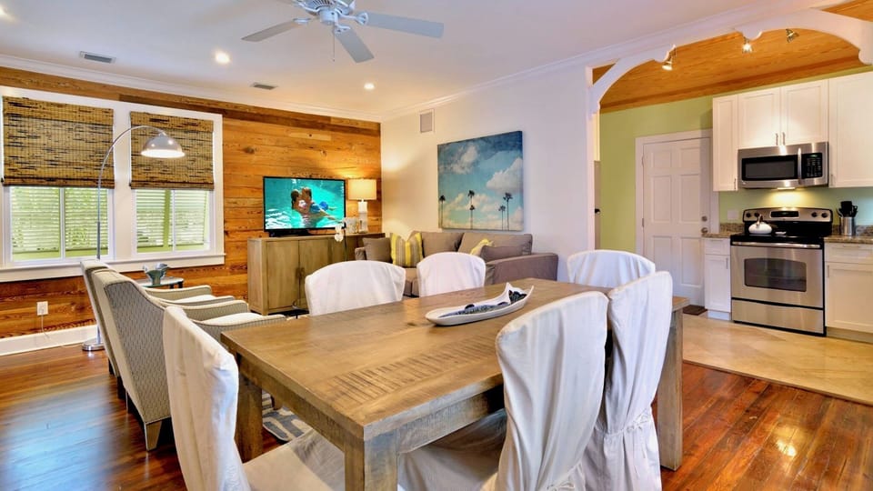 Gather around the handcrafted dining table and sink into comfortable chairs. The open layout flows from dining to living space, with gleaming wood floors and coastal artwork creating a breezy, welcoming vibe.