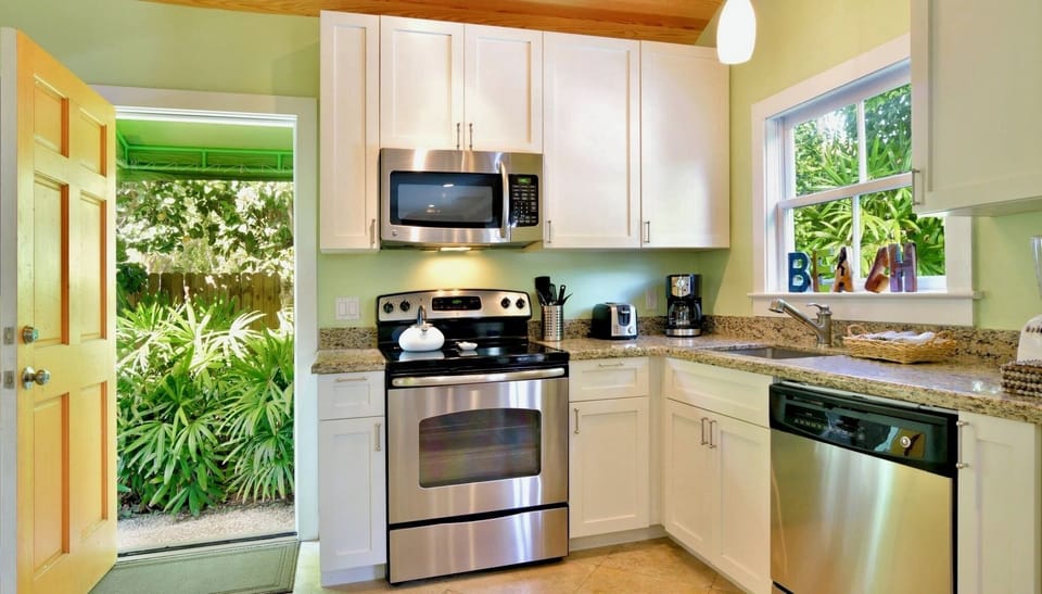 Your fully equipped kitchen awaits with modern stainless steel appliances, granite counters, and cheerful green walls that catch natural light from garden views through both windows.