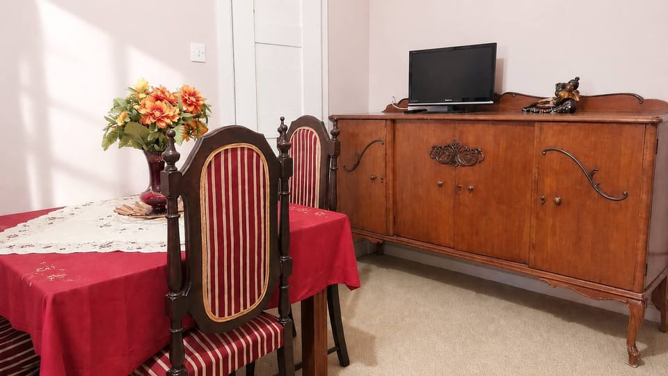 A traditional dining space with vintage wooden cabinetry, elegant chairs, warm decorative accents and a TV 